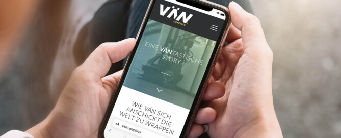 Handybildschirm der Firmengeschichte VÄN graphics mit Schoß und Händen im Hintergrund
