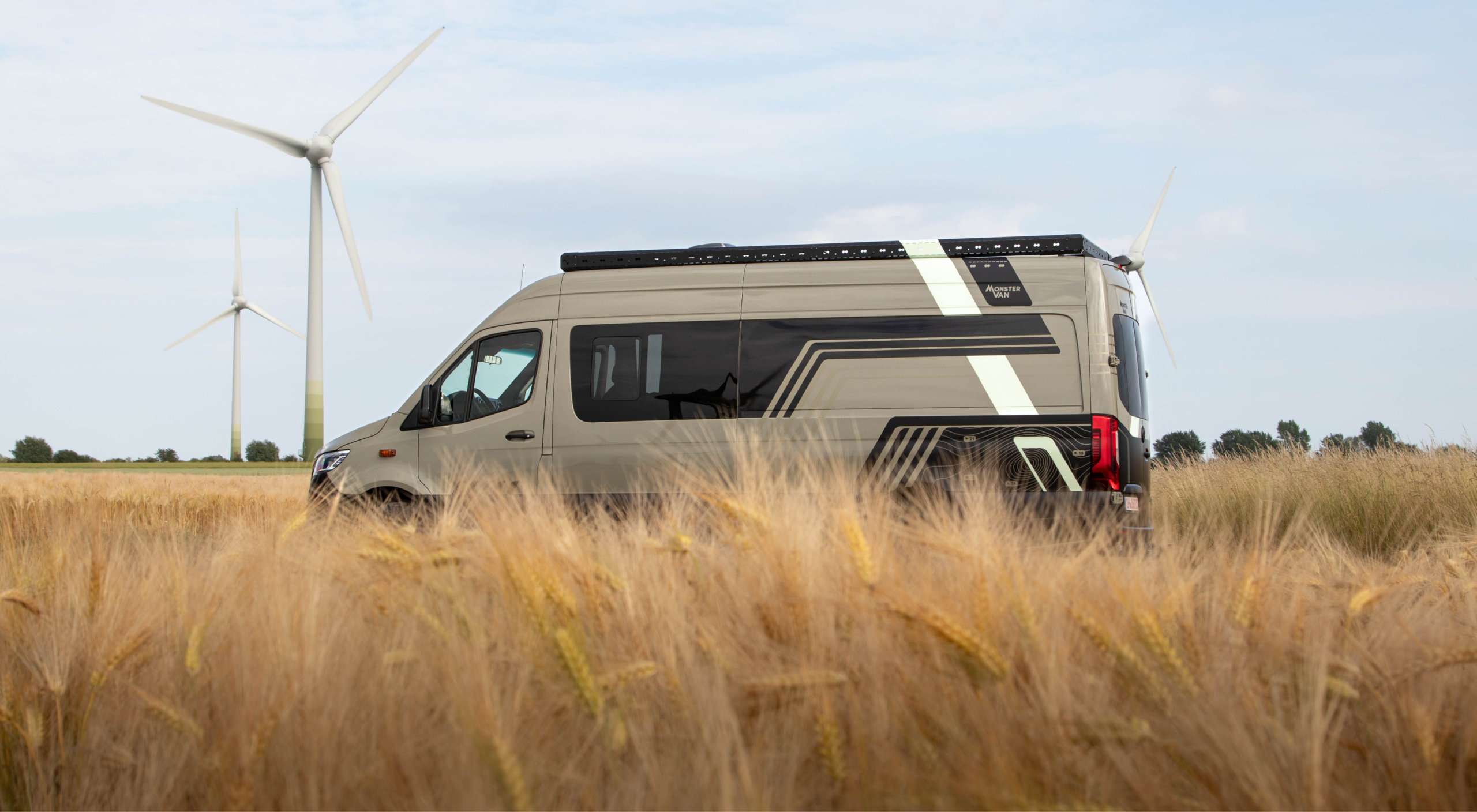 Mercedes Sprinter Camper – Designfolierung im modernen Adventure-Look in der Natur Mercedes Sprinter Camper mit individueller Folierung in Landschaft mit Windrädern