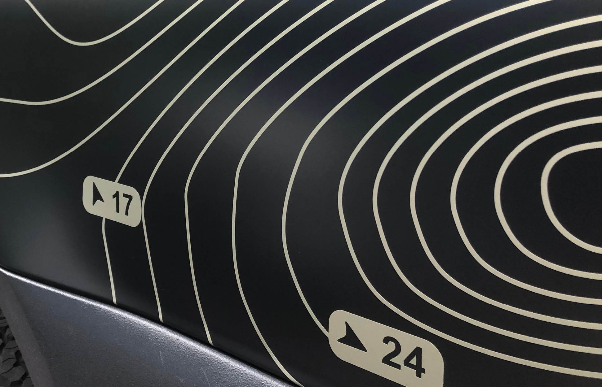 Camper Folierung mit topografischem Muster – präzise Designarbeit im Detail Detailaufnahme einer Fahrzeugfolierung mit topografischem Linienmuster in Beige auf schwarzem Untergrund