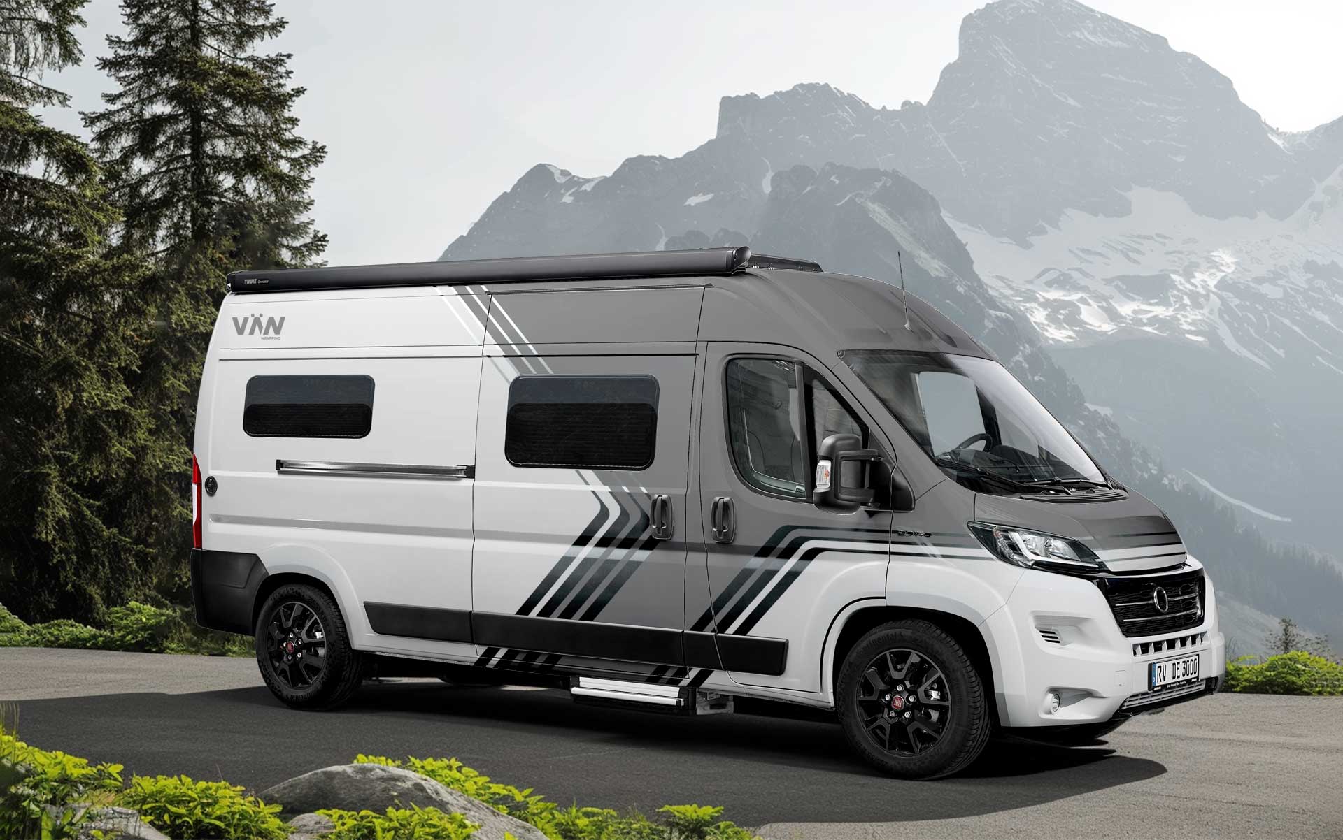 VÄN Camper mit moderner Grau-Weiß-Folierung und grafischen Linien, geparkt vor einer Berglandschaft mit Felsen und Nadelbäumen