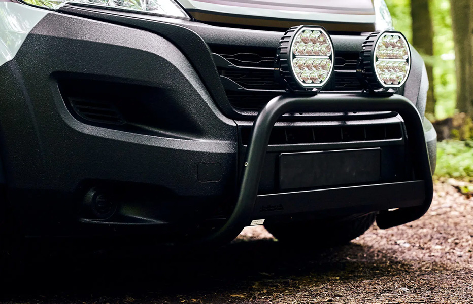 Vorderdetail mit Licht von Fiat Ducato Camper mit schwarzen Linien und braun/weißer Folierung im Wald