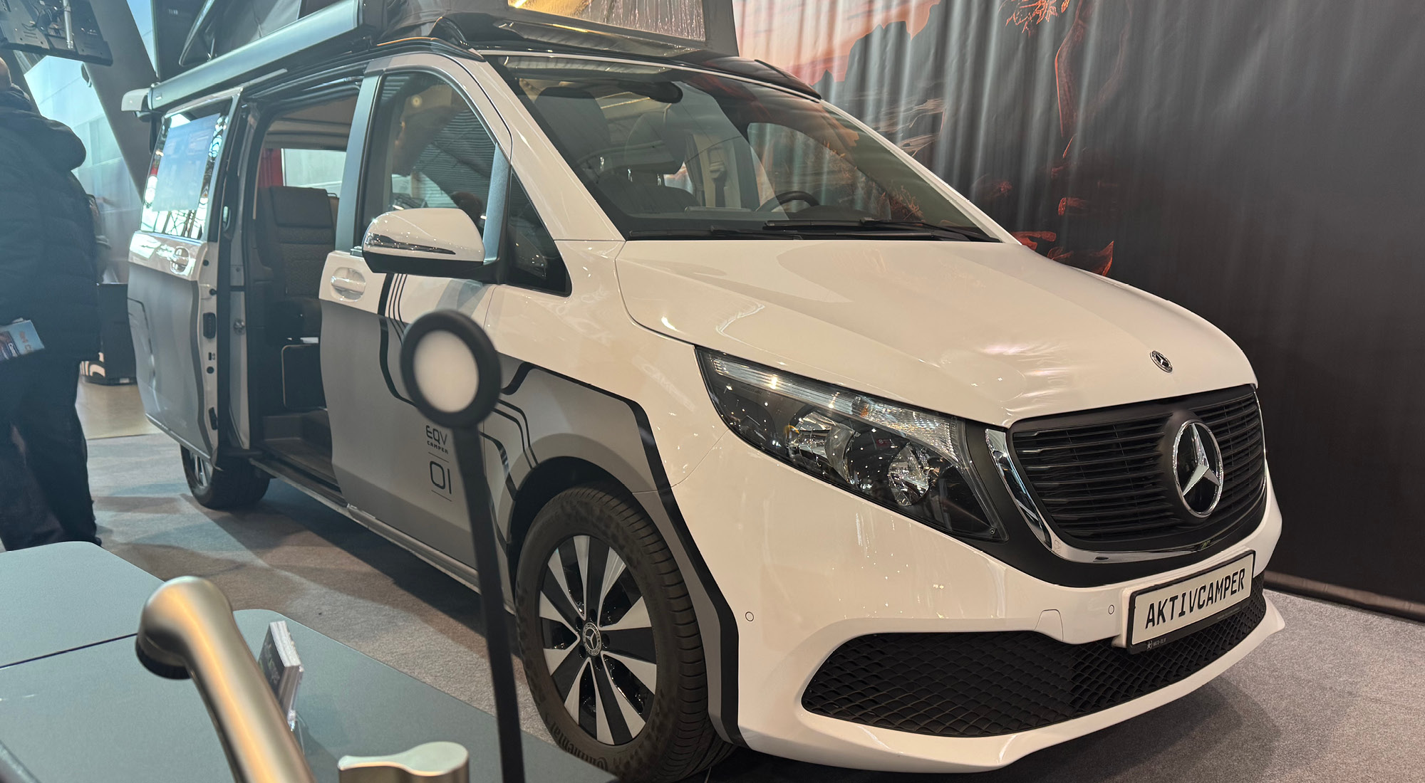 Vorderansicht Mercedes EQV Elektro Camper mit modernem Linienmuster in Grau weiß mit offener Tür auf Messe