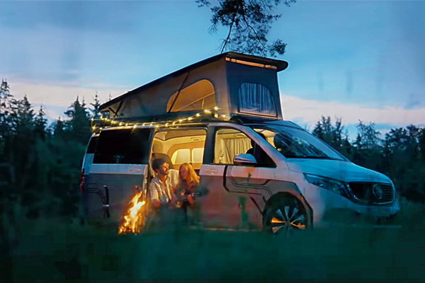 Mercedes EQV Elektro Camper mit modernem Linienmuster in Grau weiß – in abendlicher Stimmung beim Campen mit einem Pärchen mit Wald im Hintergrund