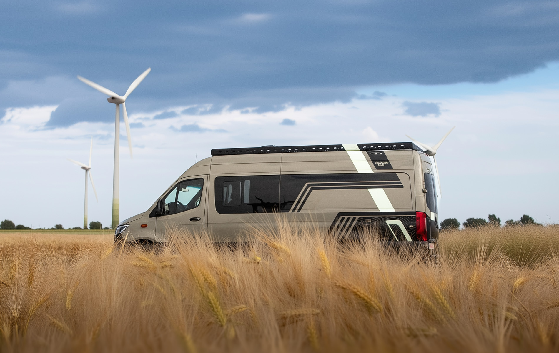 Seitenansicht von Mercedes Sprinter Camper mit schwarz/weißen Linien und sandfarbener Folierung im Feld mit Windrädern im Hintergrund